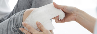 A bandage or dressing being placed or wrapped onto a knee.