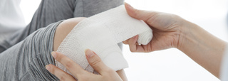 A bandage or dressing being placed or wrapped onto a knee.