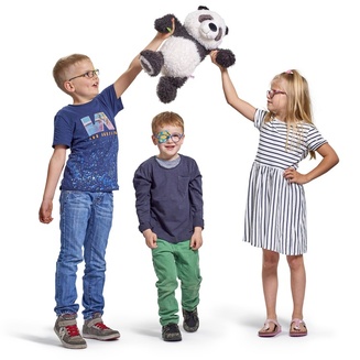 Kinder spielen mit einem Teddy Pandabär. Junge in der Mitte trägt das ORTOPAD® Augenokklusionspflaster mit dem Motiv "Emoticons" auf einem Auge.