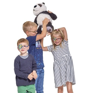 Drei Kinder mit verschiedenen ORTOPAD® Augenokklusionspflastern spielen mit Pandabär