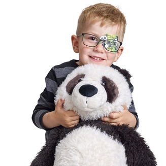 Niño con parche de oclusión ocular ORTOPAD® “Oso panda” sostiene un peluche panda con el brazo