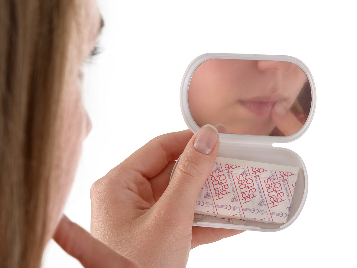 Woman placing herpes patch on lip with help of handheld mirror
