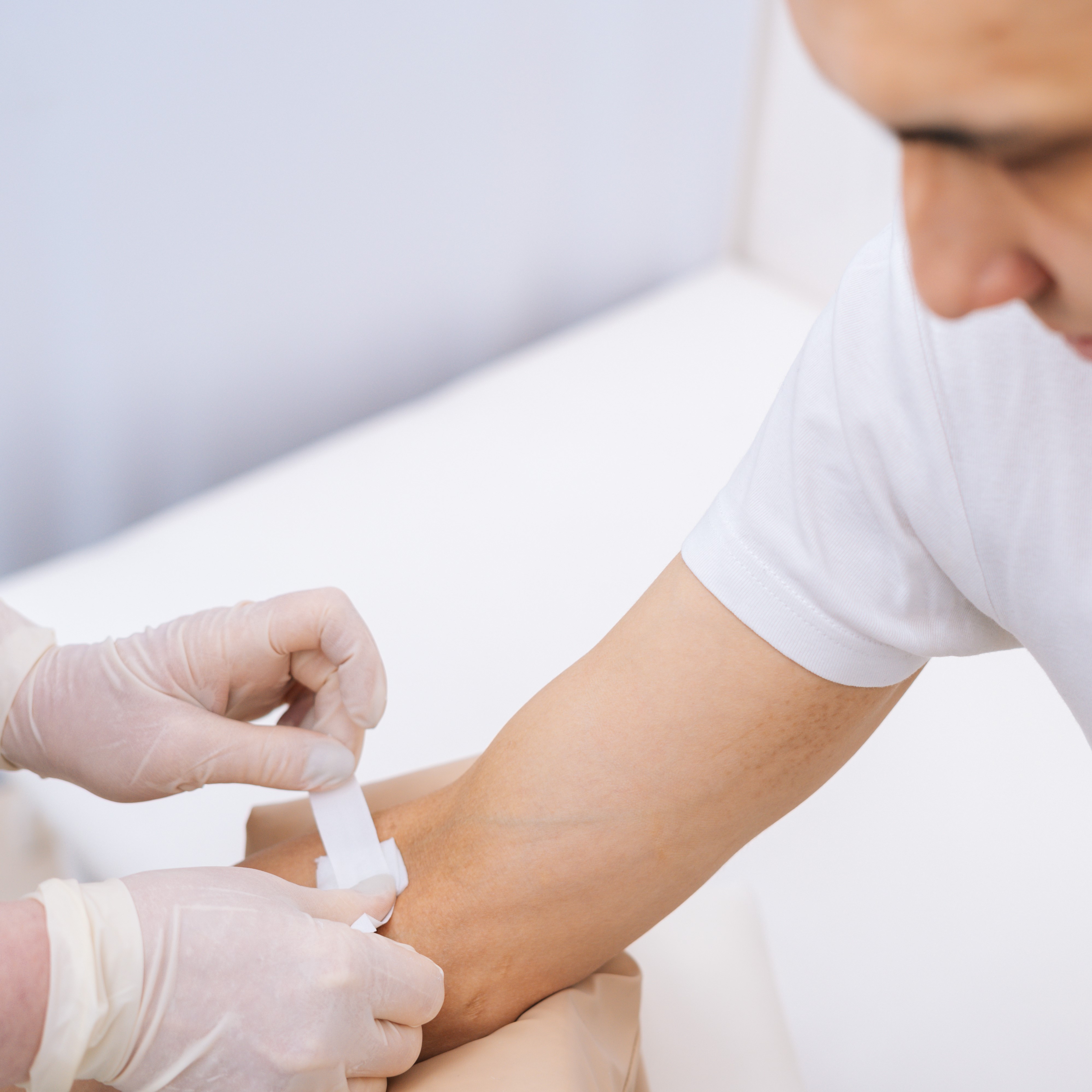 A swab is being fixated in the inside of a man’s elbow with a plaster roll 